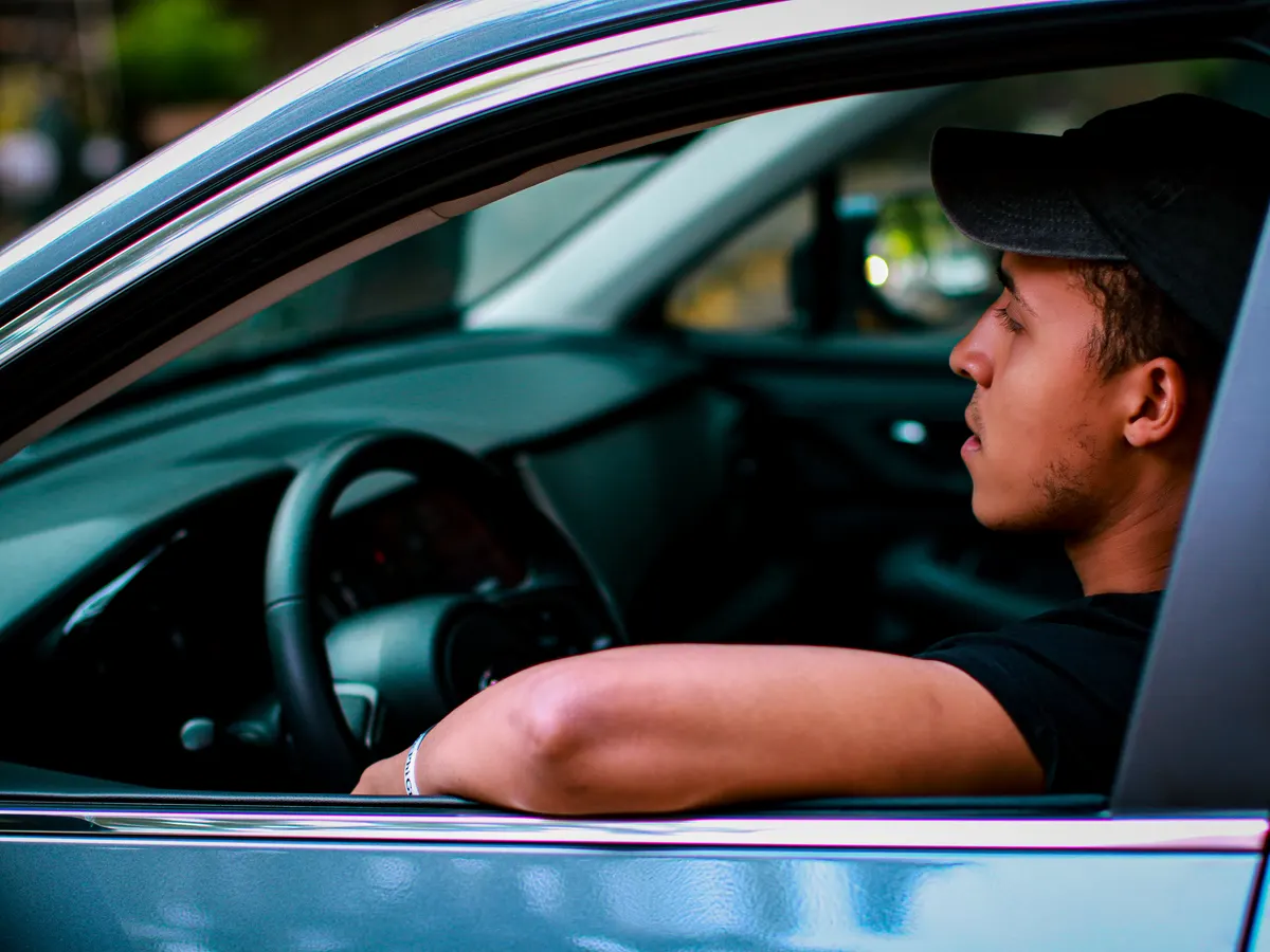Man driving a car, seen through the open driver’s window